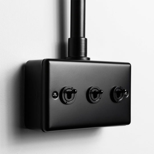 Matt Black 3 Gang 2 Way Toggle Switch With Back Box And Conduit On Light Grey Background