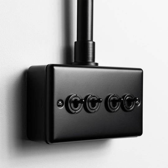 Matt Black 4 Gang 2 Way Toggle Switch  With Back Box And Conduit On Light Grey Wall