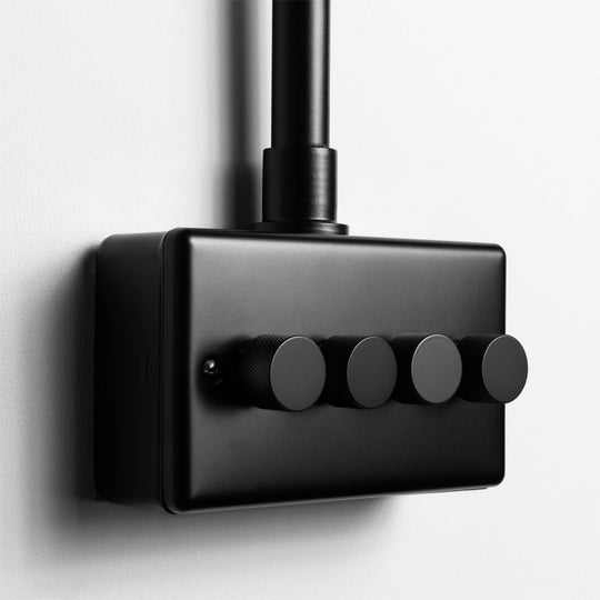 Matt Black 4 Gang LED Dimmer Switch With Back Box And Conduit On A Light Grey Background