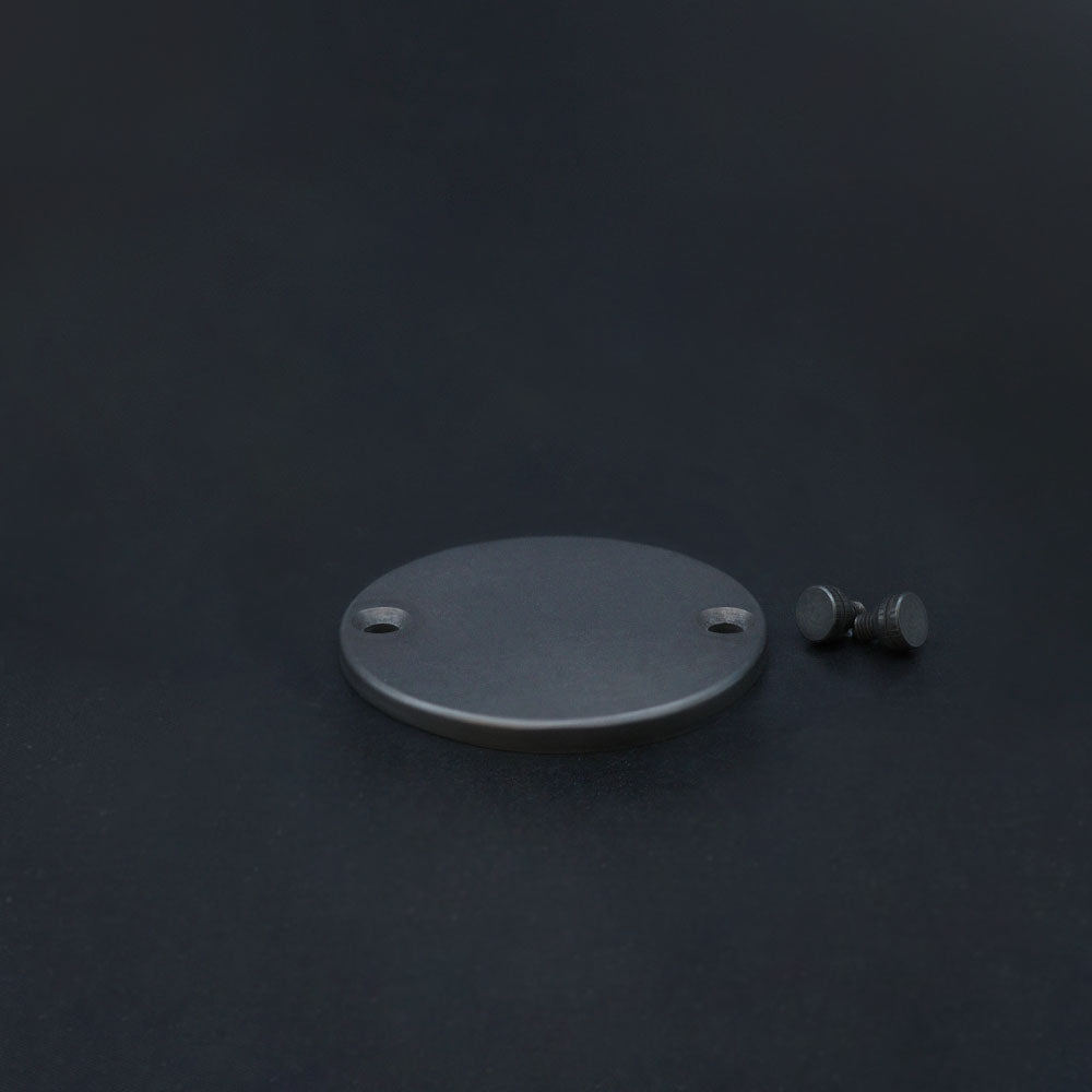 A dark bronze metal conduit box lid alongside its mounting screws, placed on a dark background.