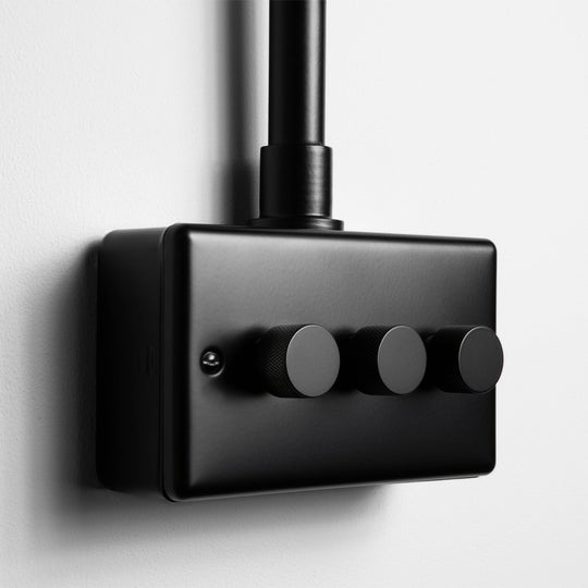 Matt Black 3 Gang 2 Way LED Dimmer Switch With Back Box And Conduit On A Light Grey Background