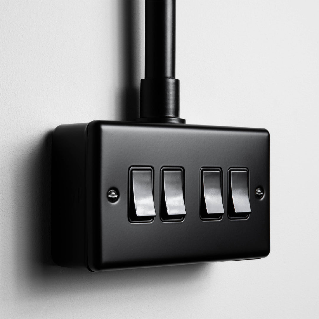 Matt Black 4 Gang 2 Way Switch With Back Box And Conduit On A Light Grey Background